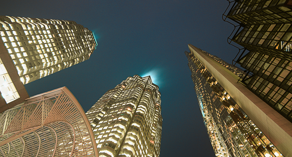 Downtown skyscrapers illuminated at night, shot from below against dark blue sky.