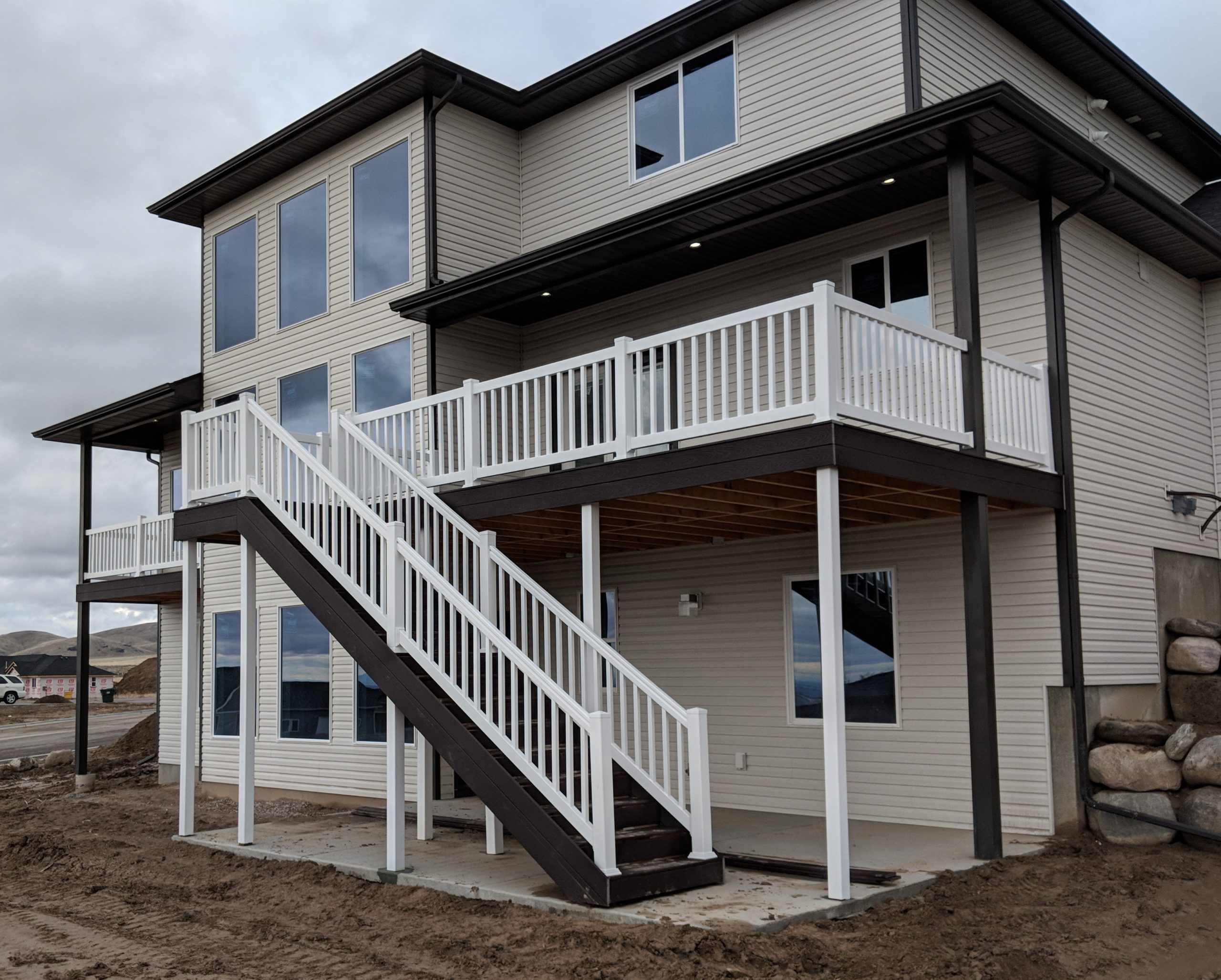 Upgrade your home's exterior with a custom multi-story composite deck by DeckPro LLC. Pictured here, this expansive new construction features clean white railings and columns, contrasting with dark brown composite steps and decking. We designed a wide, sturdy staircase to connect the upper levels directly to the lower level concrete patio, maximizing both access and outdoor living space.