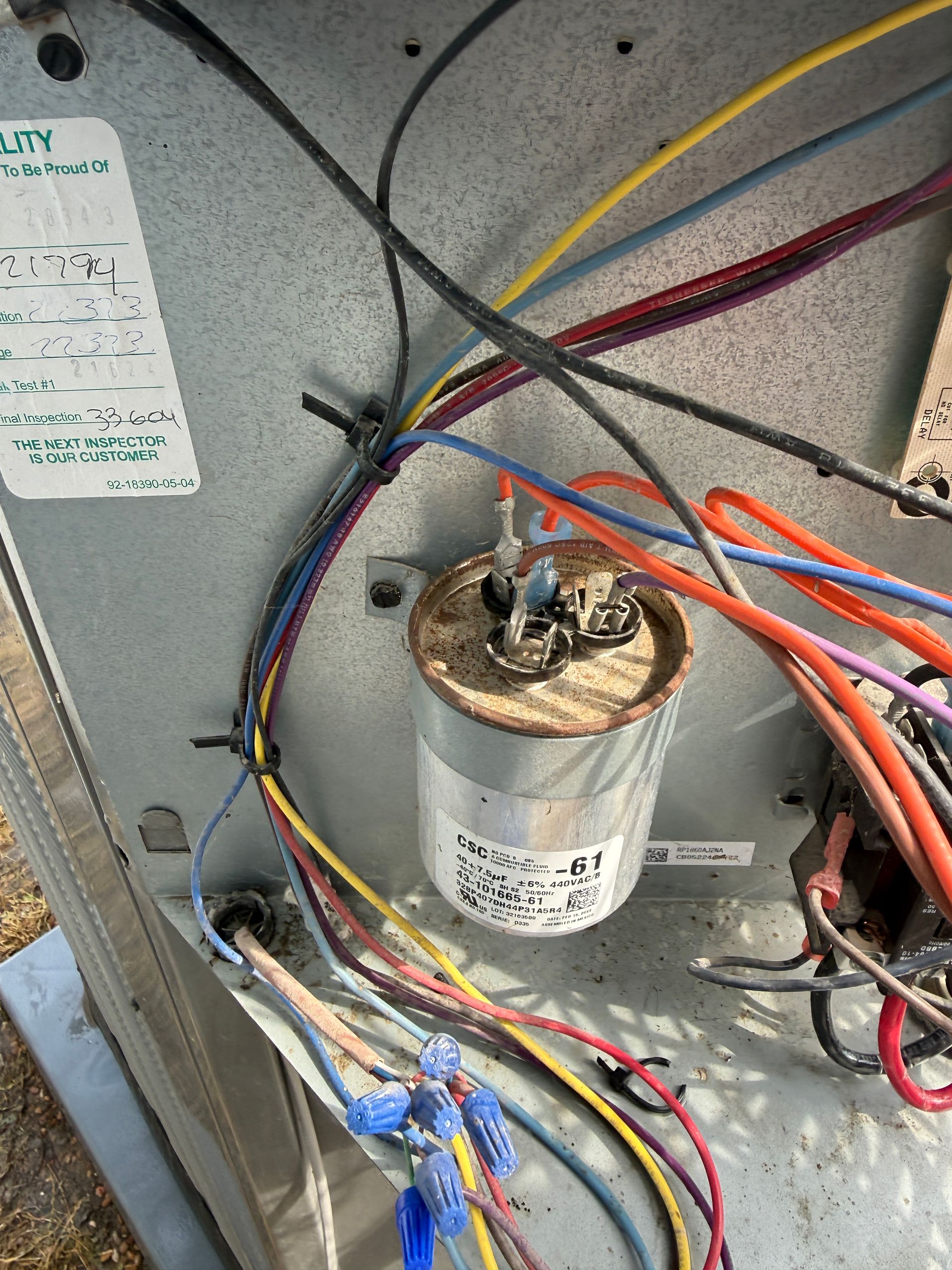 Close-up of HVAC capacitor and wiring connections inside condenser unit. Shows electrical components, terminals, and bundled wires used in system operation, highlighting repair or diagnostic work.