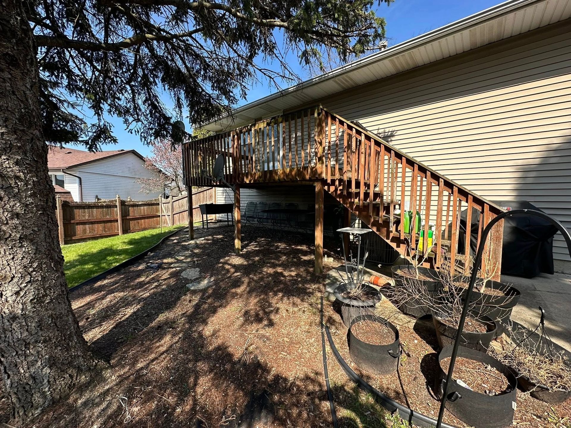 An elevated wooden backyard deck provides outdoor entertainment space with stairs, railing, and structural supports, demonstrating durable residential construction, functional design, and convenient access between home and yard.