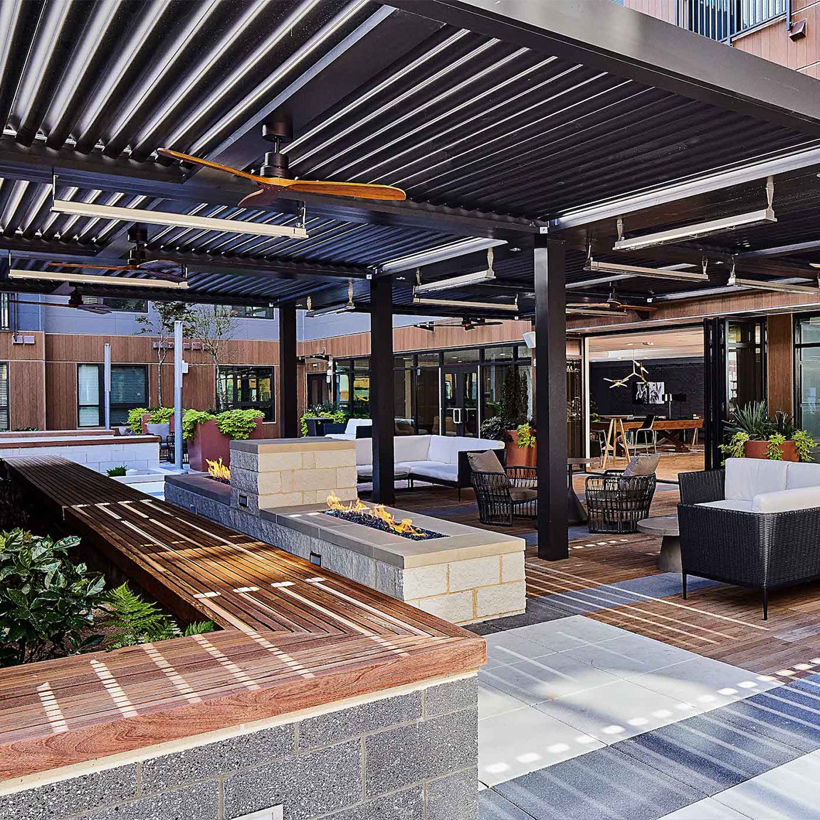 Large-scale motorized louvered pergola with integrated radiant heaters, ceiling fans, and a linear gas fire feature for a commercial outdoor lounge space