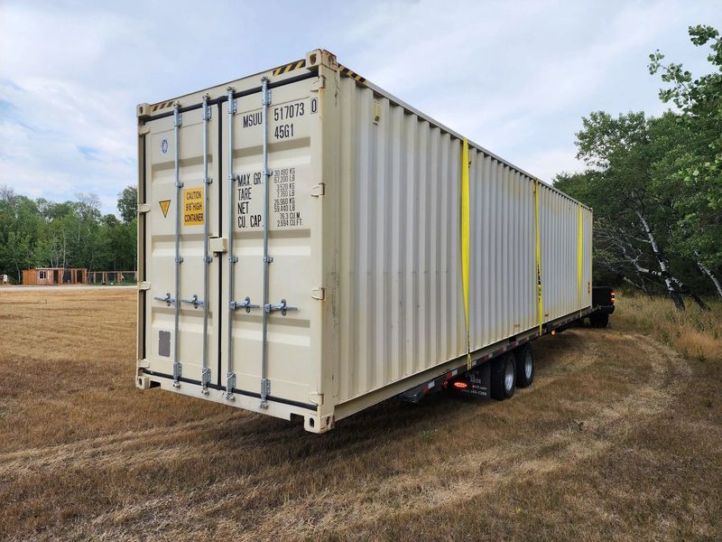 Large portable storage container secured on trailer in outdoor field, featuring durable steel construction and locking doors, ideal for long-term storage, transport, and protection of equipment or belongings.