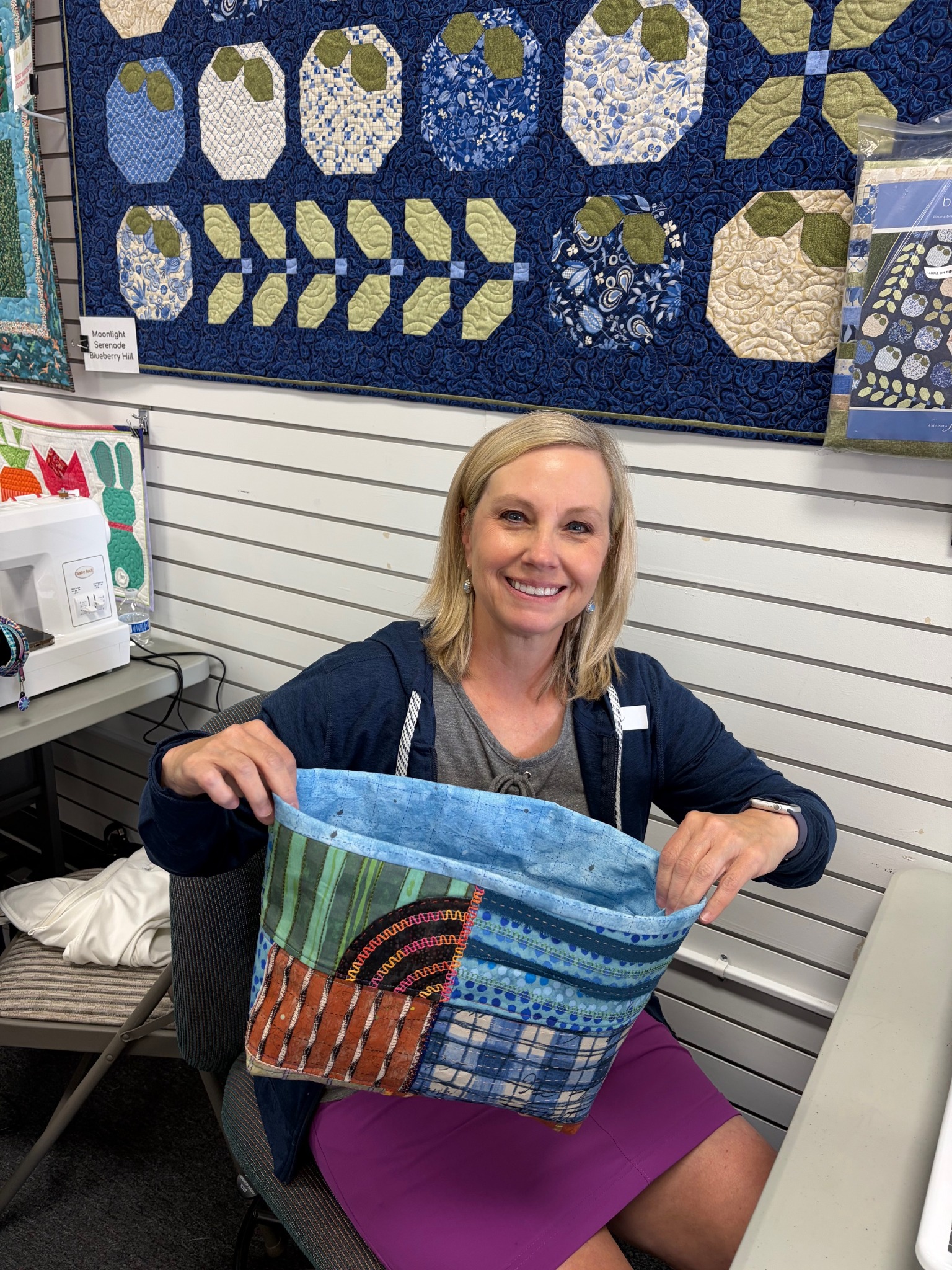 A student proudly displays her handmade patchwork fabric basket after a Decorative Stitch class. This creative sewing project highlights decorative stitching, fabric piecing, and practical techniques for making beautiful storage baskets.