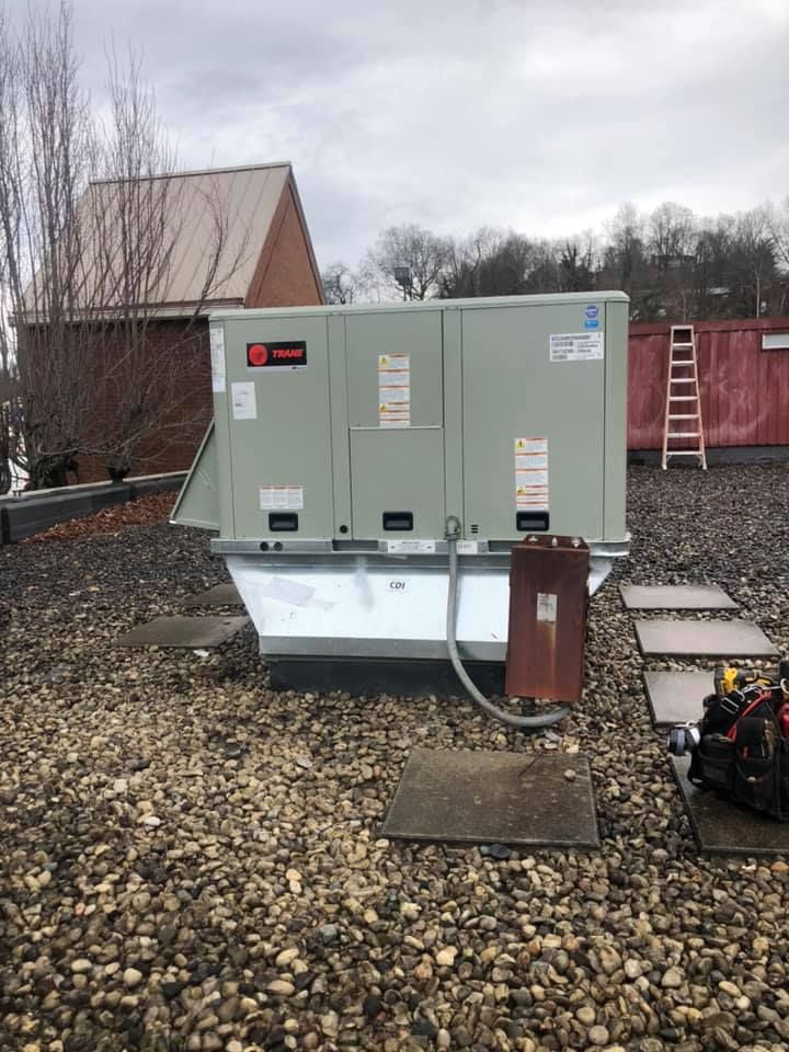 Trane rooftop HVAC unit installed on commercial building with gravel surface, featuring electrical connections and service panel access, representing professional heating and cooling system setup, maintenance readiness, and reliable climate control equipment.