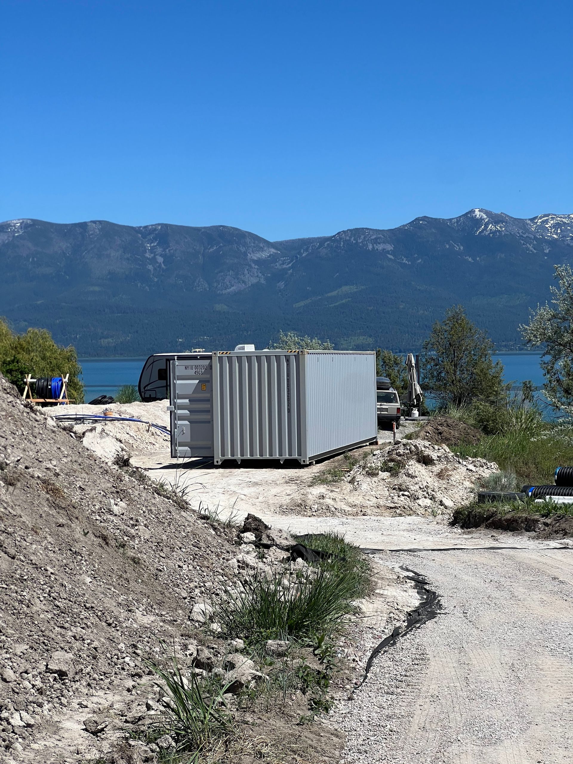 Portable storage container placed at construction site near lake with mountain backdrop, showcasing secure onsite storage solution for tools, materials, and equipment in scenic residential or commercial project locations.