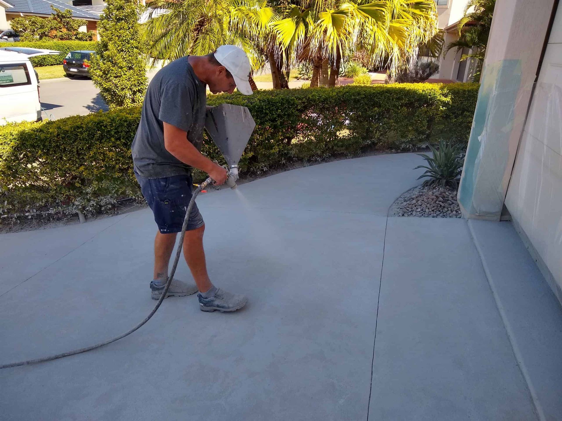 Technician applies surface coating on residential concrete pathway using spray equipment, ensuring smooth finish, improved durability, and enhanced appearance for outdoor surfaces in landscaping and home improvement projects.