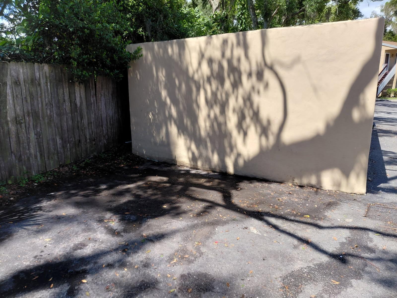 A clean, cleared asphalt parking space alongside a beige wall and wooden fence following junk remova 