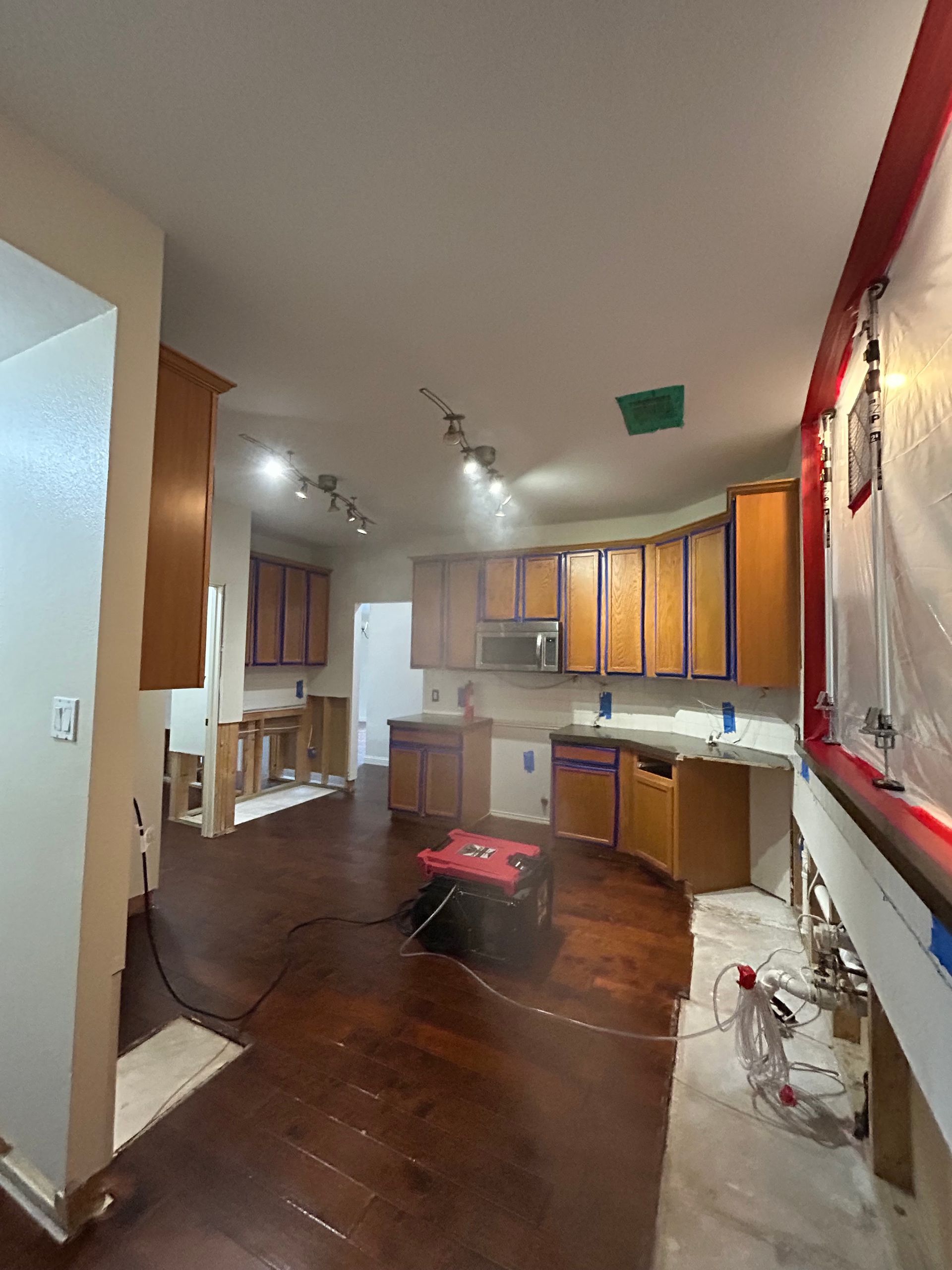 A residential kitchen undergoing restoration features taped cabinetry, exposed wall sections, plasti 