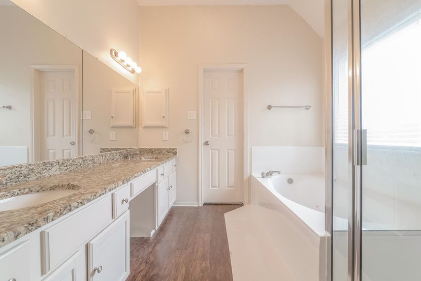 Bright bathroom with large tub and vanity with granite countertop at Invitation Homes Houston.
