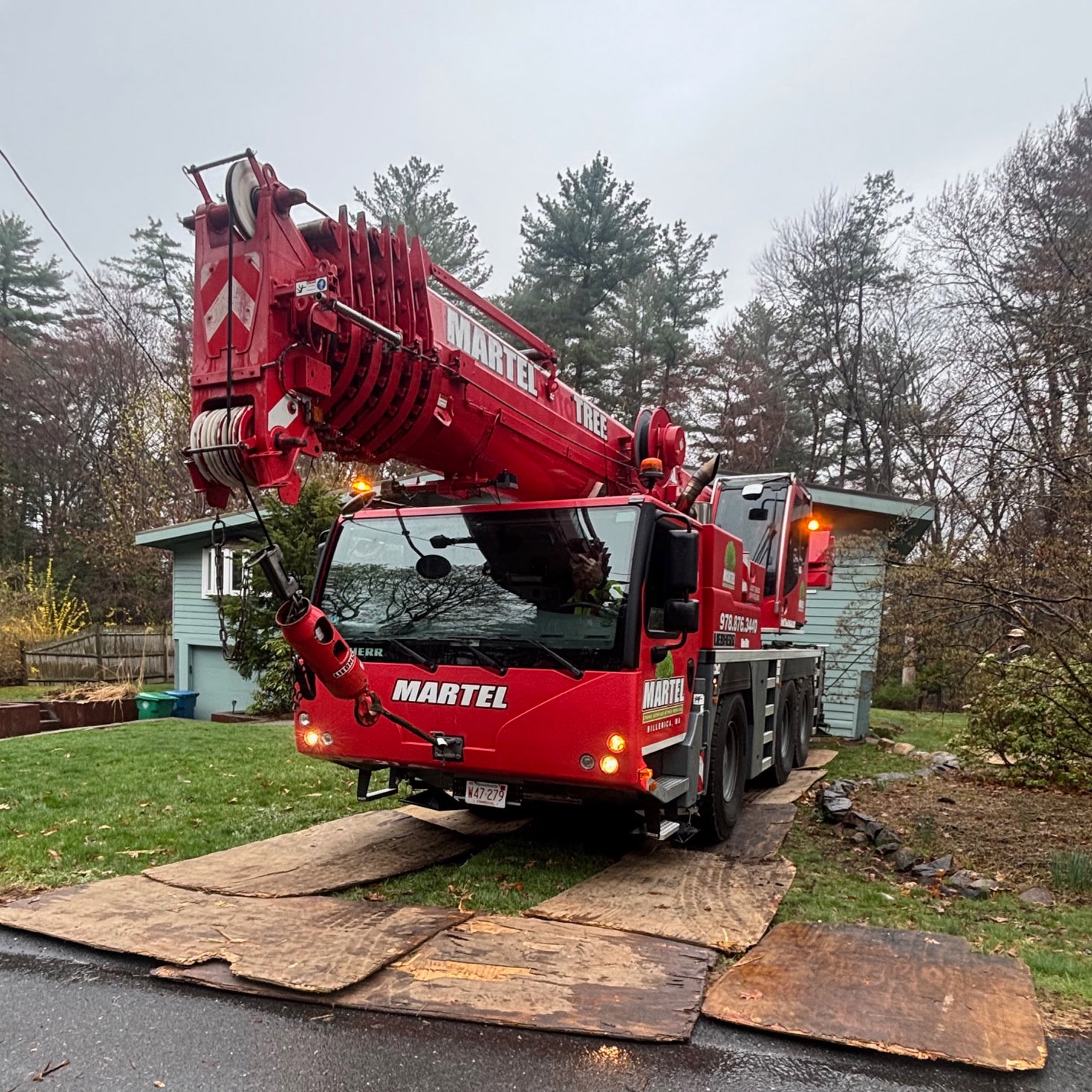 Crane-assisted tree removal project in Burlington, Massachusetts featuring front yard setup, protective mats, and precision lifting to safely remove large trees while protecting the property.