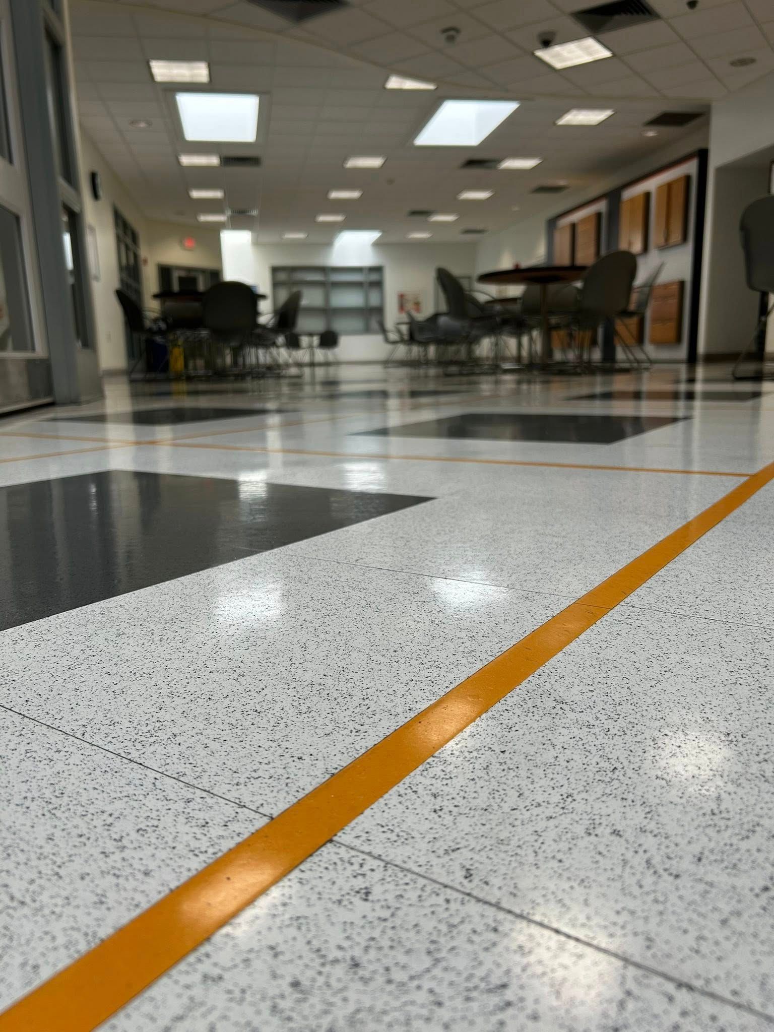 Clean, polished commercial floor in cafeteria or common area with tables and chairs, showcasing professional janitorial maintenance, reflective surface finish, and well-maintained indoor environment with organized seating and bright lighting.