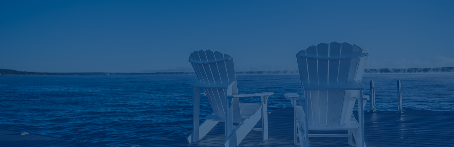 Two white Muskoka chairs on a dock facing towards a lake.