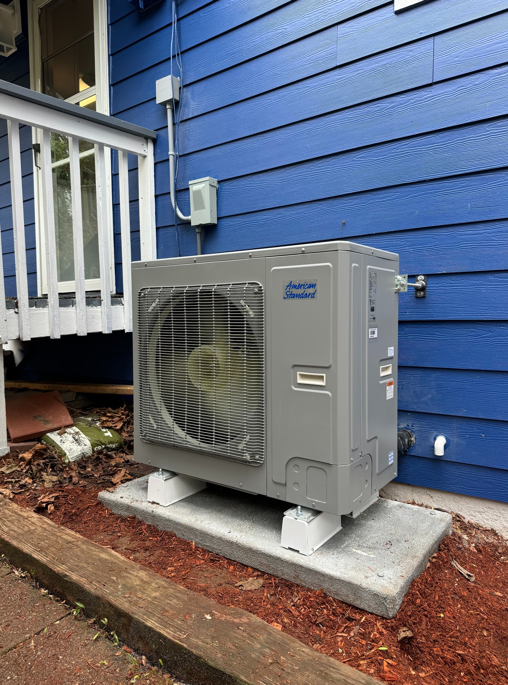 American Standard heat pump installed beside a blue home's porch. Ready Energy Solutions is a certified American Standard dealer.
