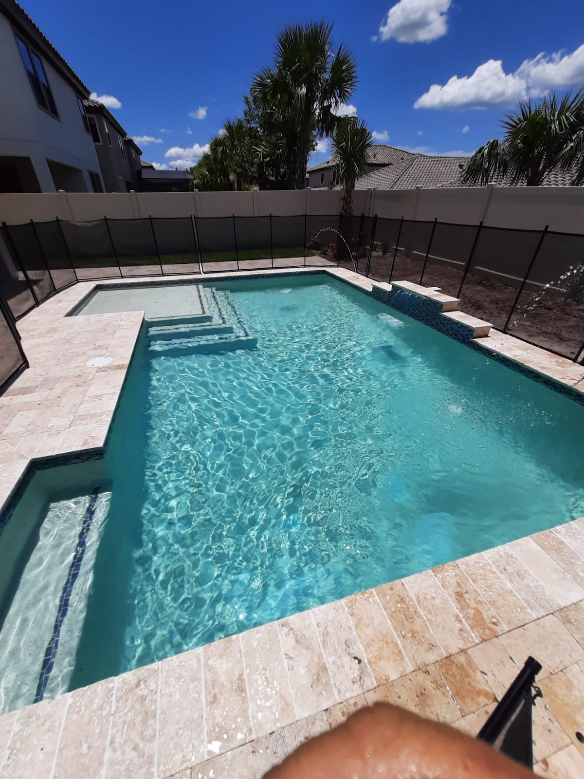 Rectangular backyard swimming pool with clear turquoise water, built-in steps, light stone decking, and a private fenced setting.