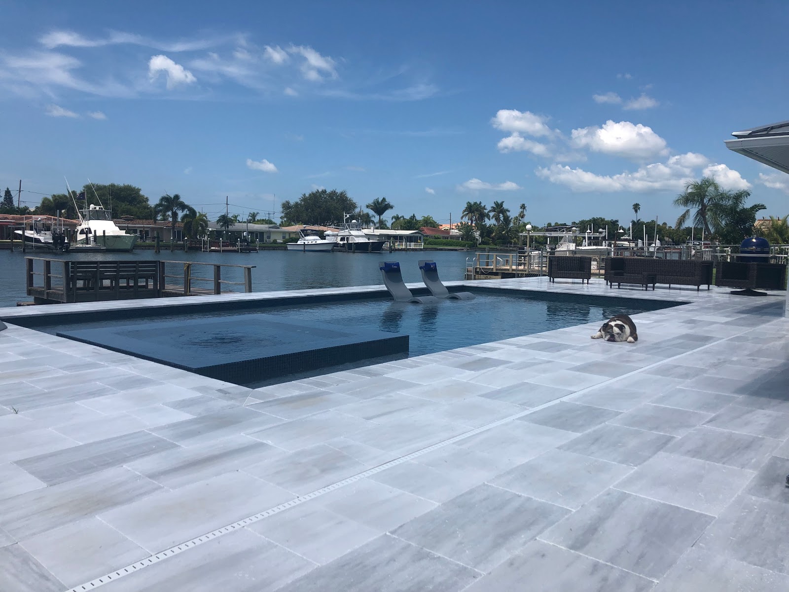Contemporary waterfront pool and patio with clean geometric lines, light stone pavers, and expansive water views.
