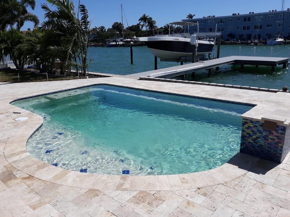 Waterfront residential swimming pool with a rounded entry area, light stone decking, and scenic canal views.