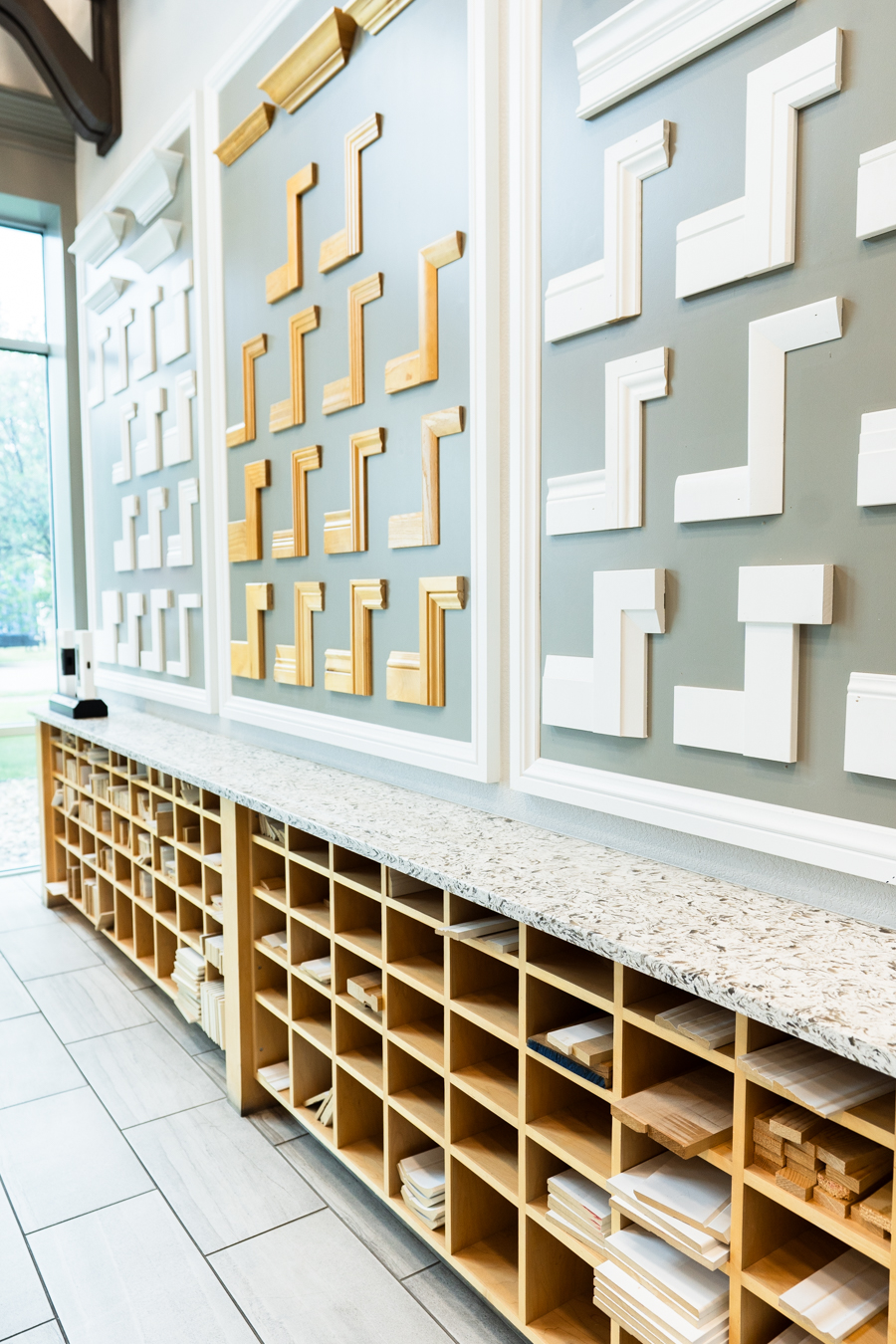 Builders FirstSource showroom with wood trim samples on display walls and organized shelves below.