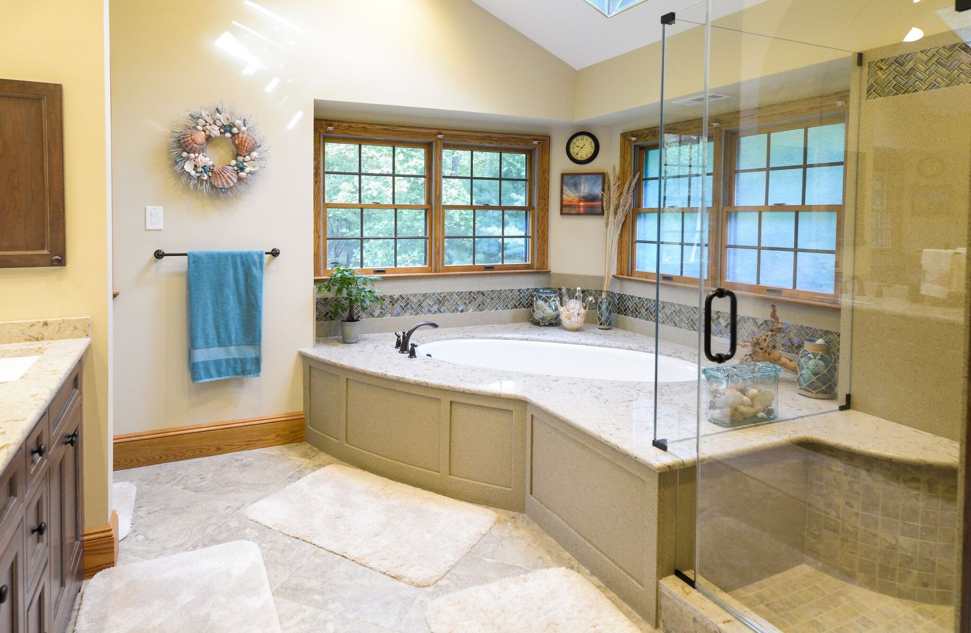 This bright bathroom features a corner-set soaking tub with a white granite surround and large windo 