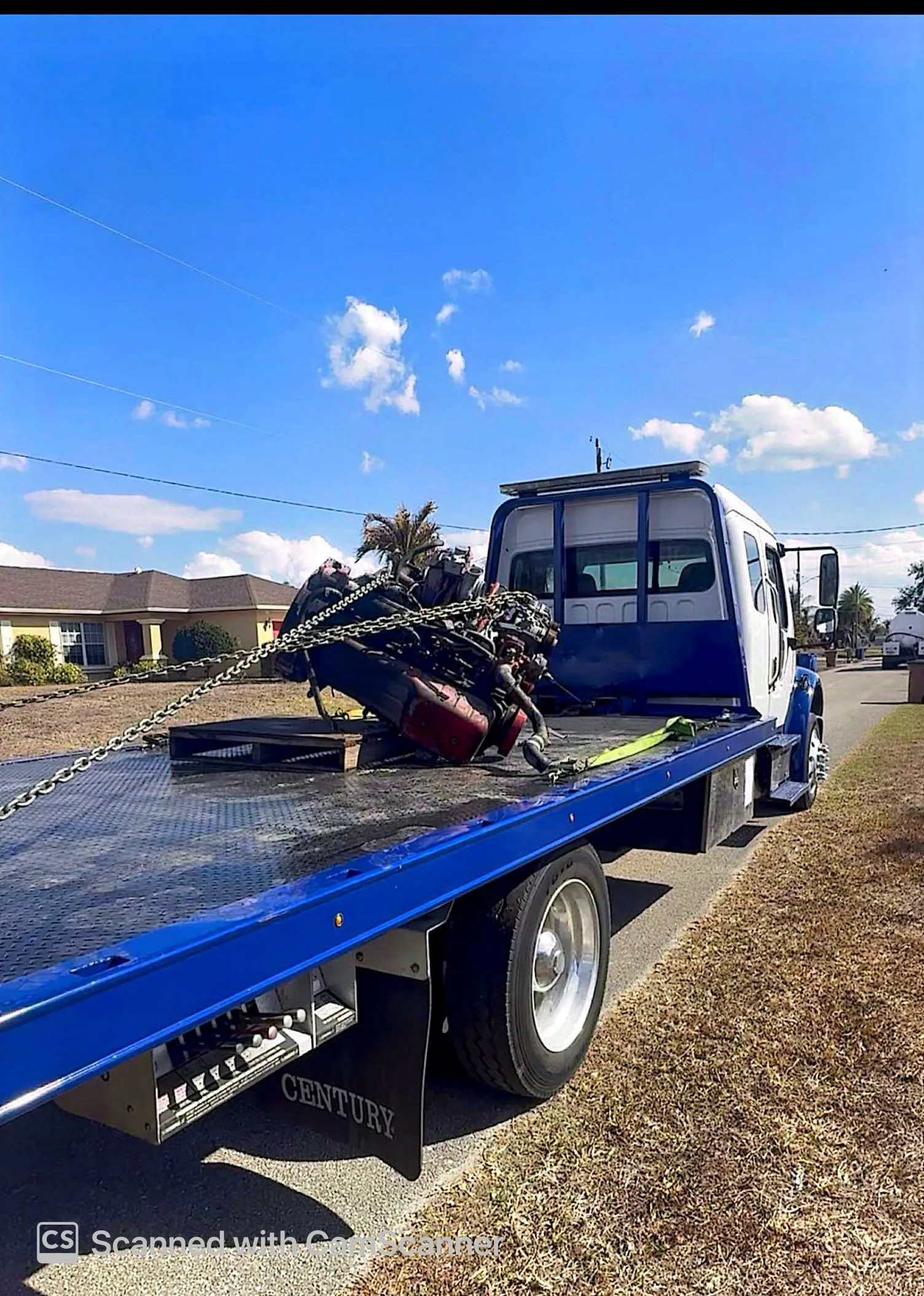A heavy automotive engine is securely chained onto a blue flatbed tow truck for specialized transport, showcasing safe loading practices, professional equipment handling, dependable hauling, and reliable roadside recovery services.