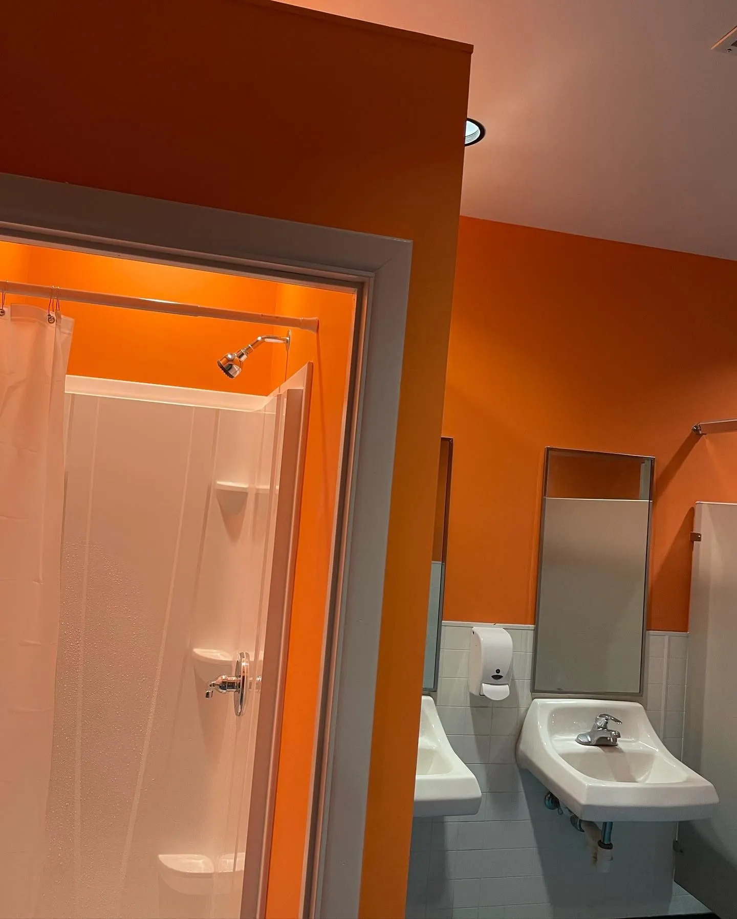 Commercial restroom featuring freshly painted orange walls, shower enclosure, wall-mounted sinks, mi 