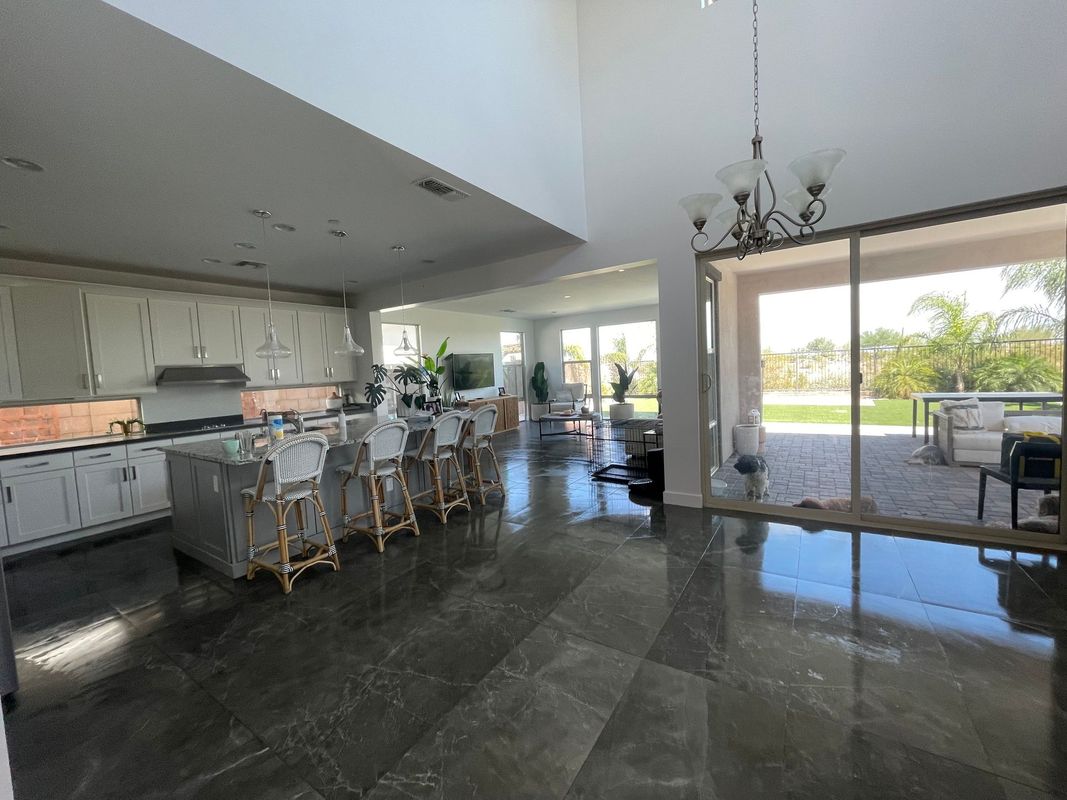 A modern open-concept kitchen and living space features a large island with bar seating, sleek cabinetry, pendant lighting, and sliding glass doors leading to a bright outdoor patio area.