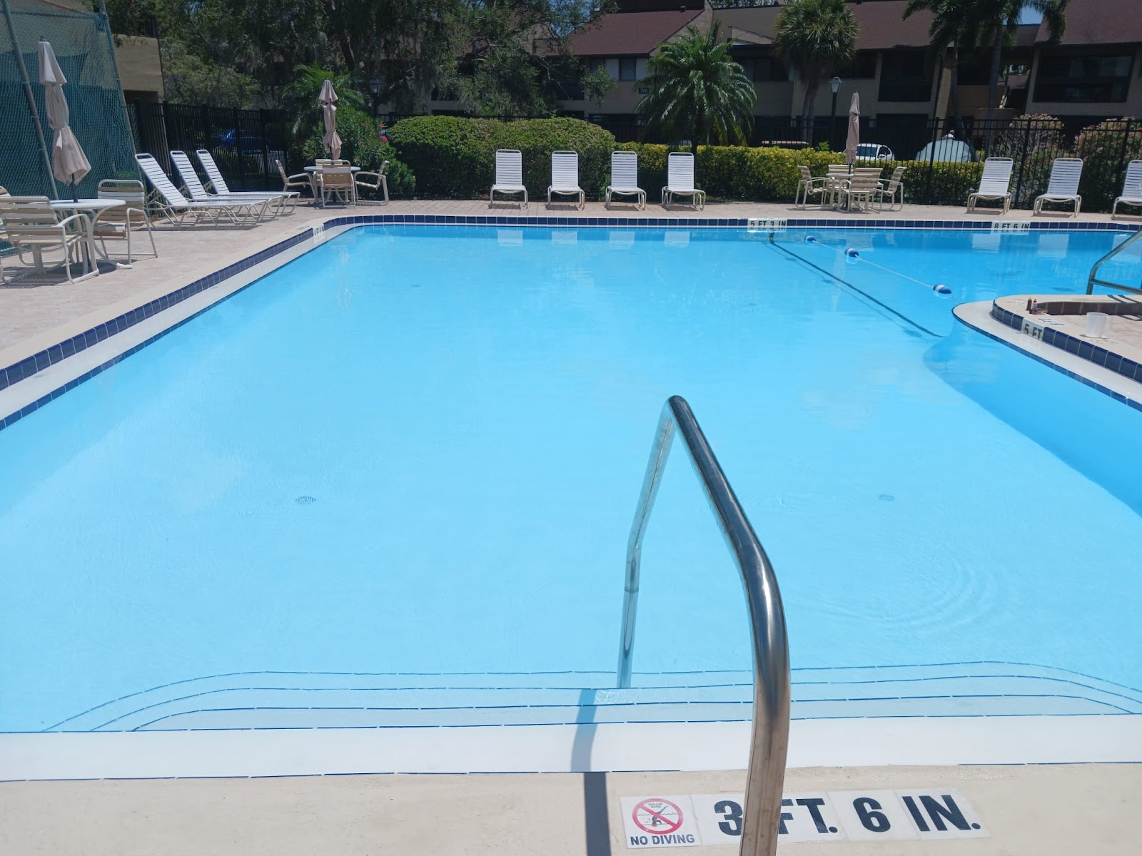 Clean residential or community swimming pool with clear blue water, wide deck space, and easy-access pool steps and handrails.