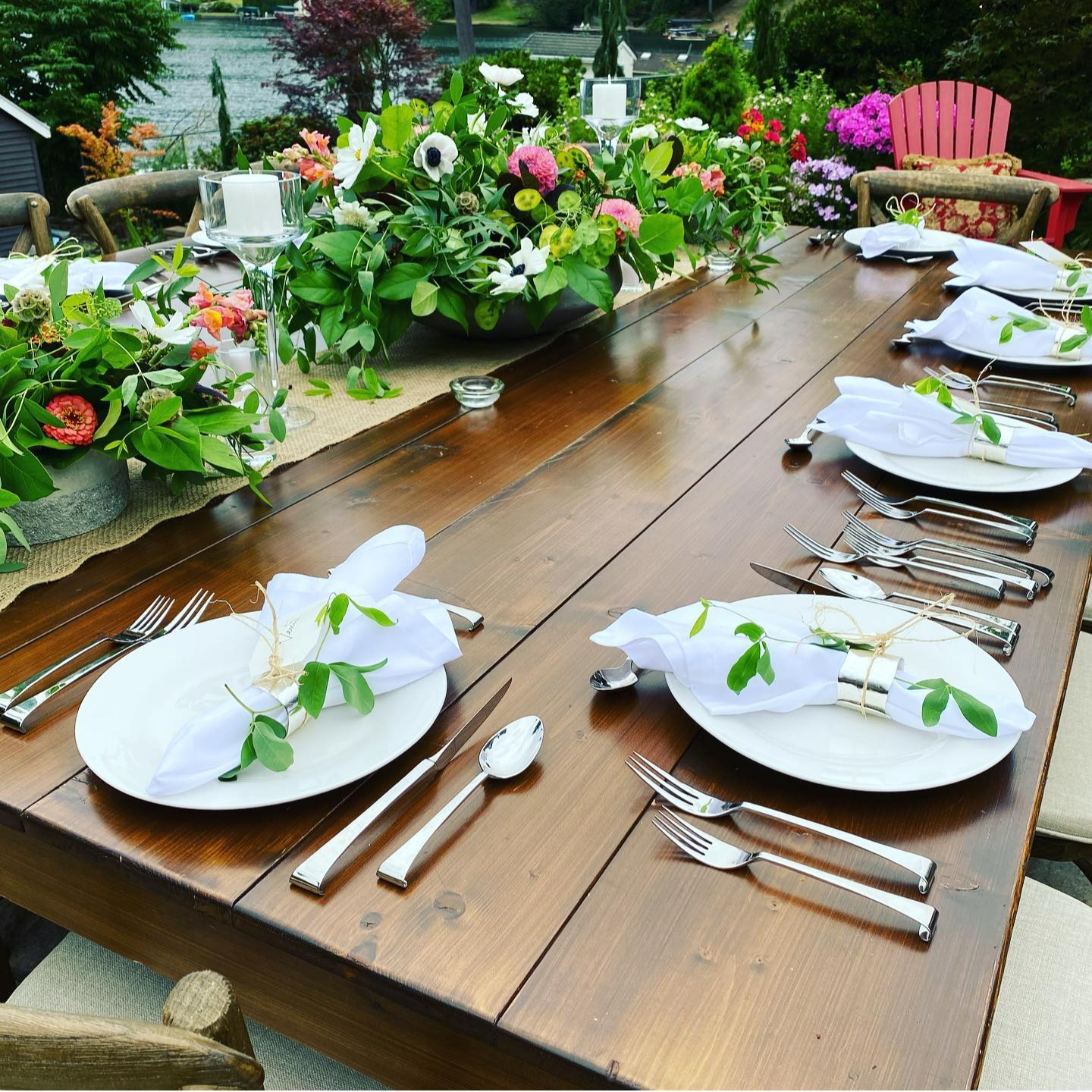 A beautifully styled outdoor dining table set for a private event catered by Chef Joe, featuring elegant white plates, polished silverware, and neatly folded napkins adorned with fresh greenery. The rustic wooden table is decorated with vibrant floral centerpieces and surrounded by lush garden scenery, creating a warm and inviting atmosphere. This setup reflects Chef Joe’s ability to transform any space into a restaurant-quality dining experience for intimate gatherings and special events throughout Phoenix, Arizona.