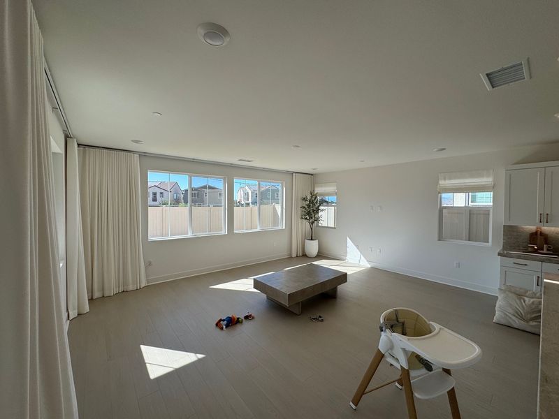 This airy living space showcases elegant floor-to-ceiling white curtains that maximize natural light. The minimalist design is completed by matching roman shades, creating a cohesive and sophisticated look throughout the home.