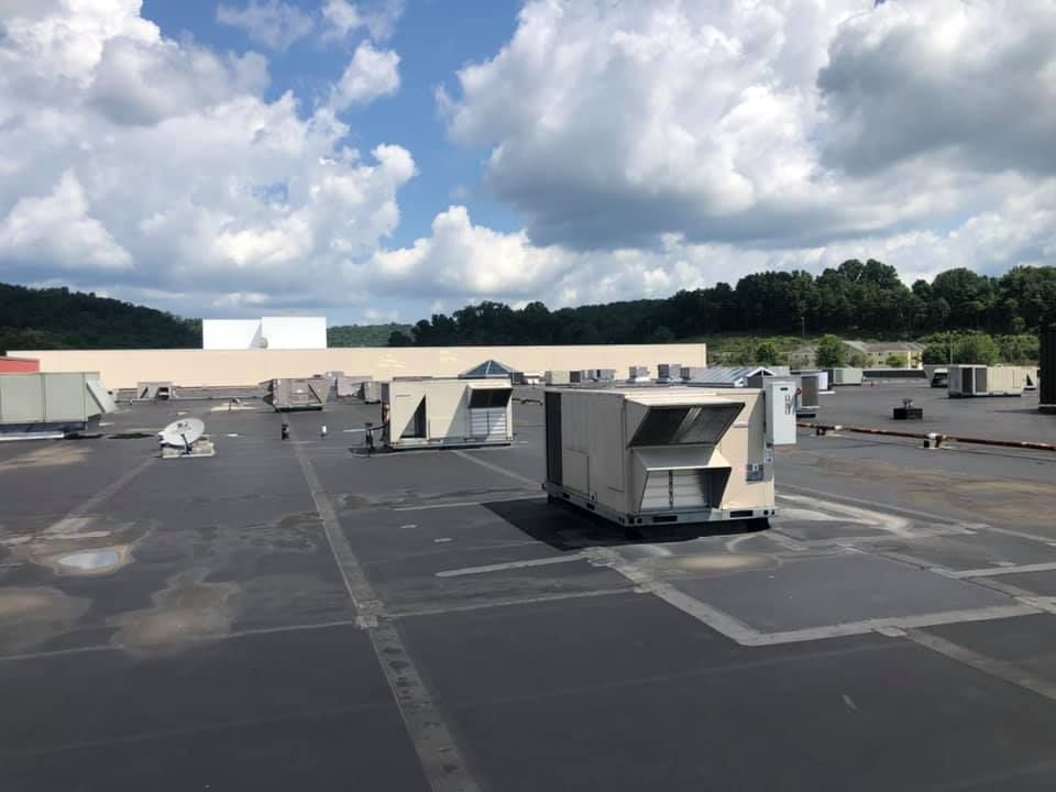 Wide view of commercial rooftop featuring multiple HVAC units spaced across flat surface, under partly cloudy sky, demonstrating large-scale heating and cooling infrastructure designed for efficient climate control and maintenance accessibility.