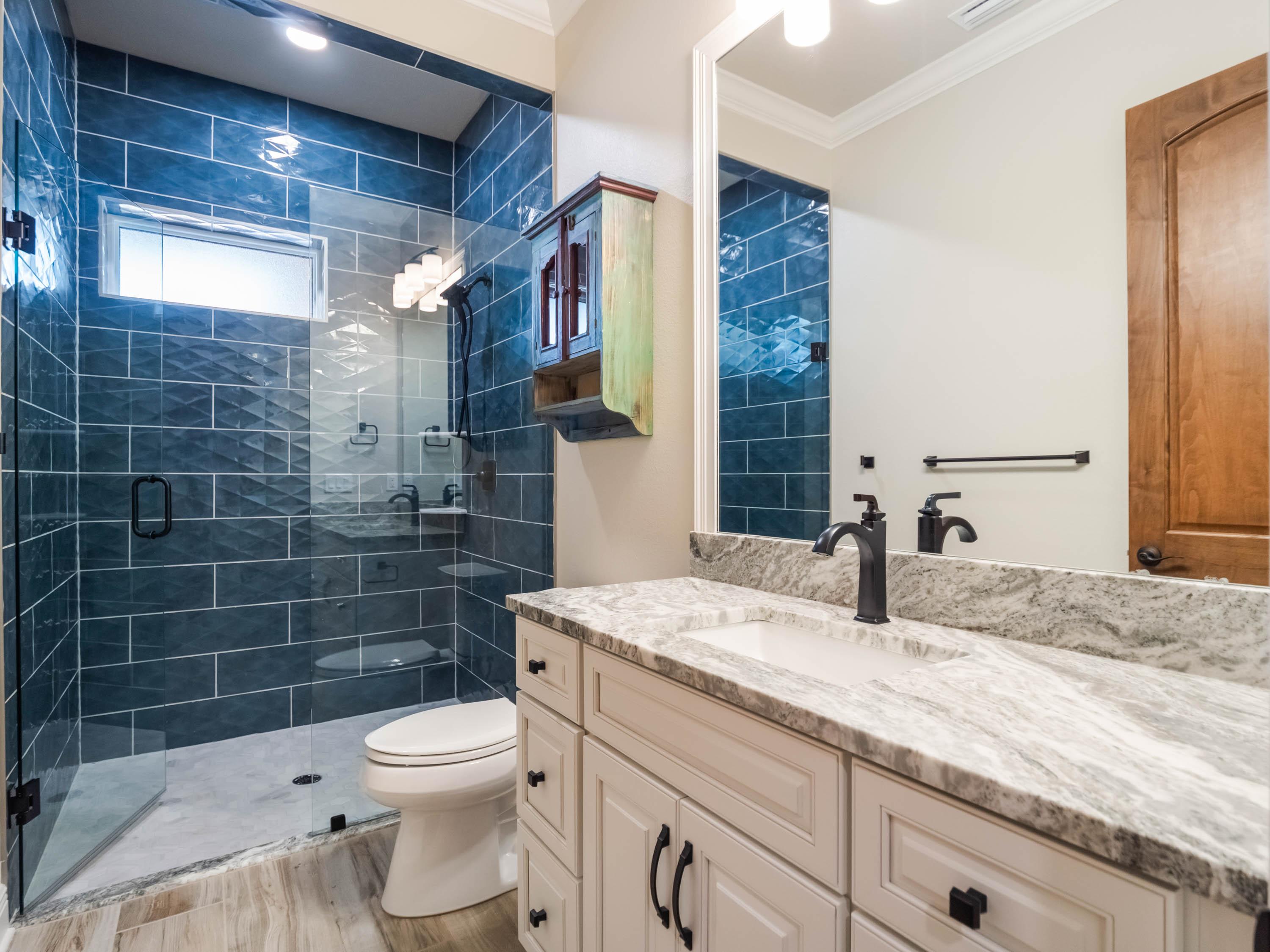 Custom bathroom in a luxury Central Florida home featuring a frameless glass shower, blue tile surround, quartz vanity countertops, and premium finishes by custom home builders in Central Florida.