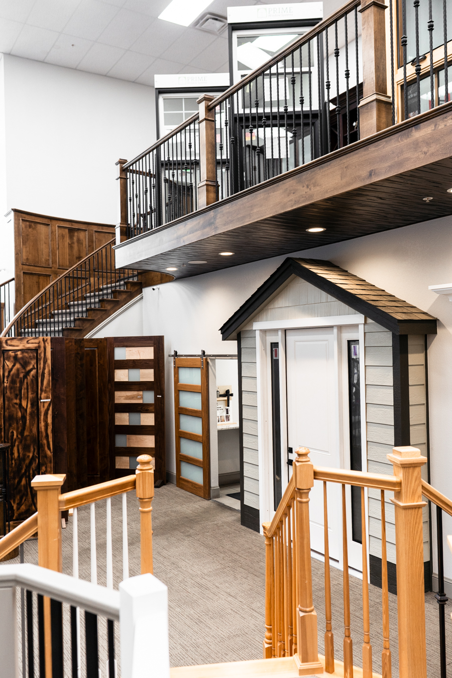 Builders FirstSource showroom with diverse doors, railings, and a small house model, showcasing construction materials.