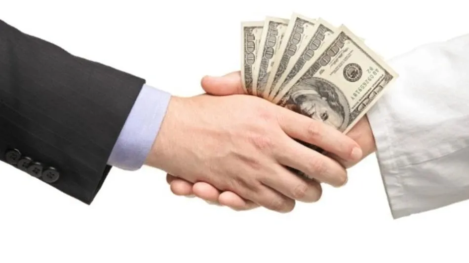Two hands are shaking, with one hand holding a fan of US dollar bills. The hand on the left is wearing a dark pinstripe suit jacket with a light blue dress shirt, and the hand on the right is wearing a white garment, possibly a doctor's coat or religious attire. The background is white, suggesting a studio setting.