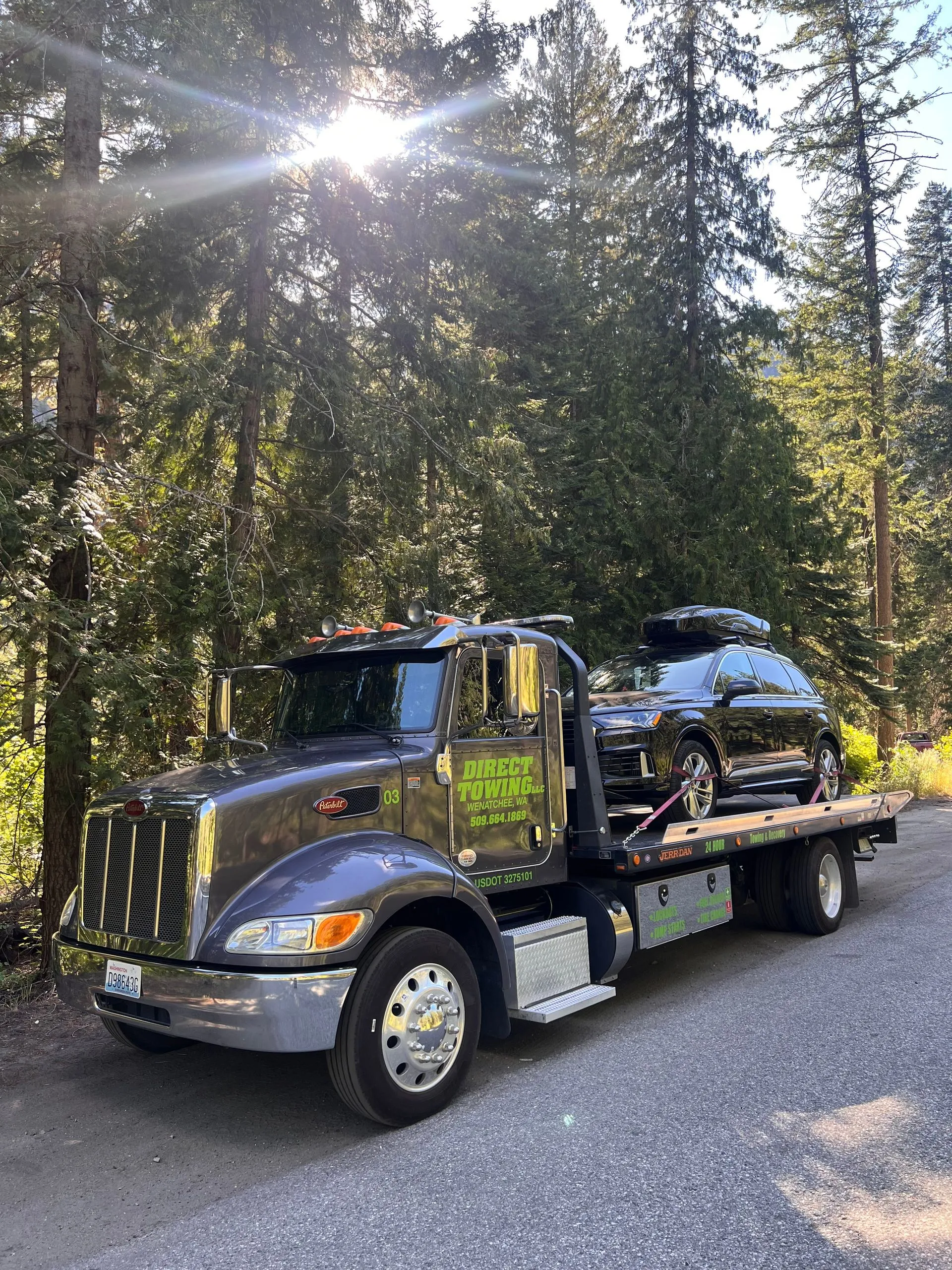 Direct Towing transporting a luxury SUV through a forested roadway, showcasing premium vehicle handling, safe transportation procedures, professional towing equipment, and reliable roadside recovery solutions.
