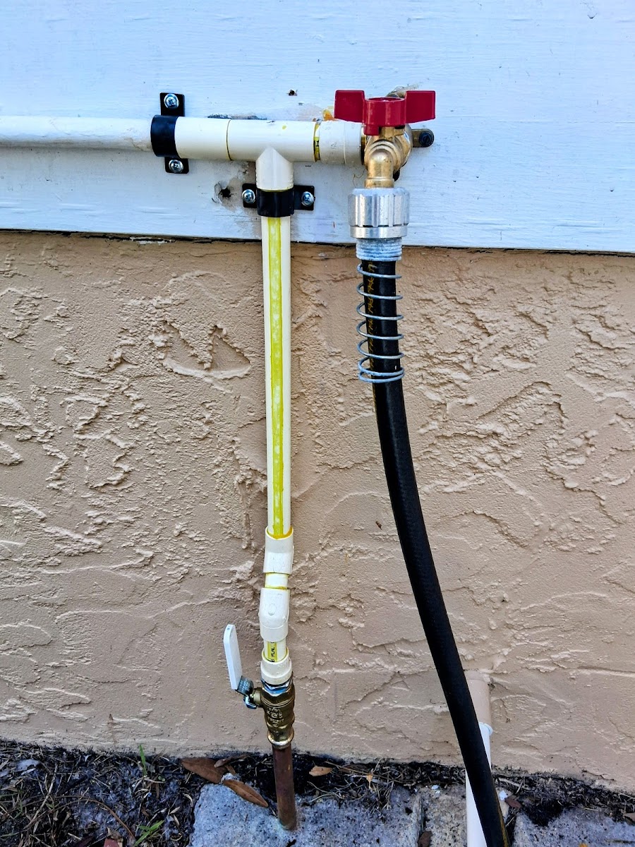 Outdoor plumbing connection with valves and piping installed on an exterior wall for water supply access.
