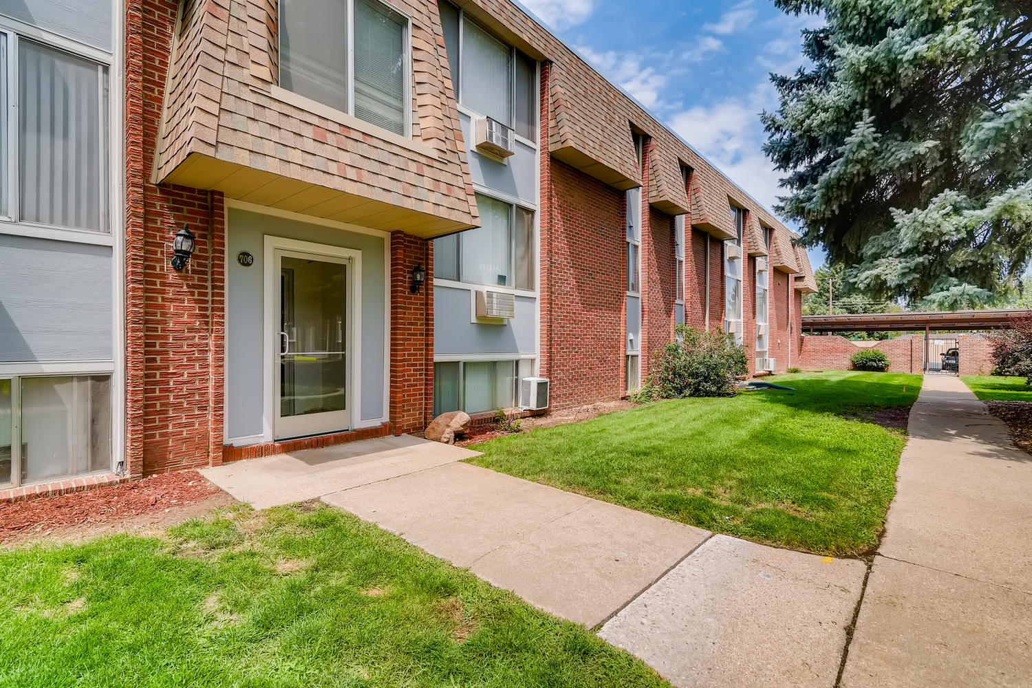 Glass door building entrance with brick and siding building exterior and grass lawn with sidewalk.