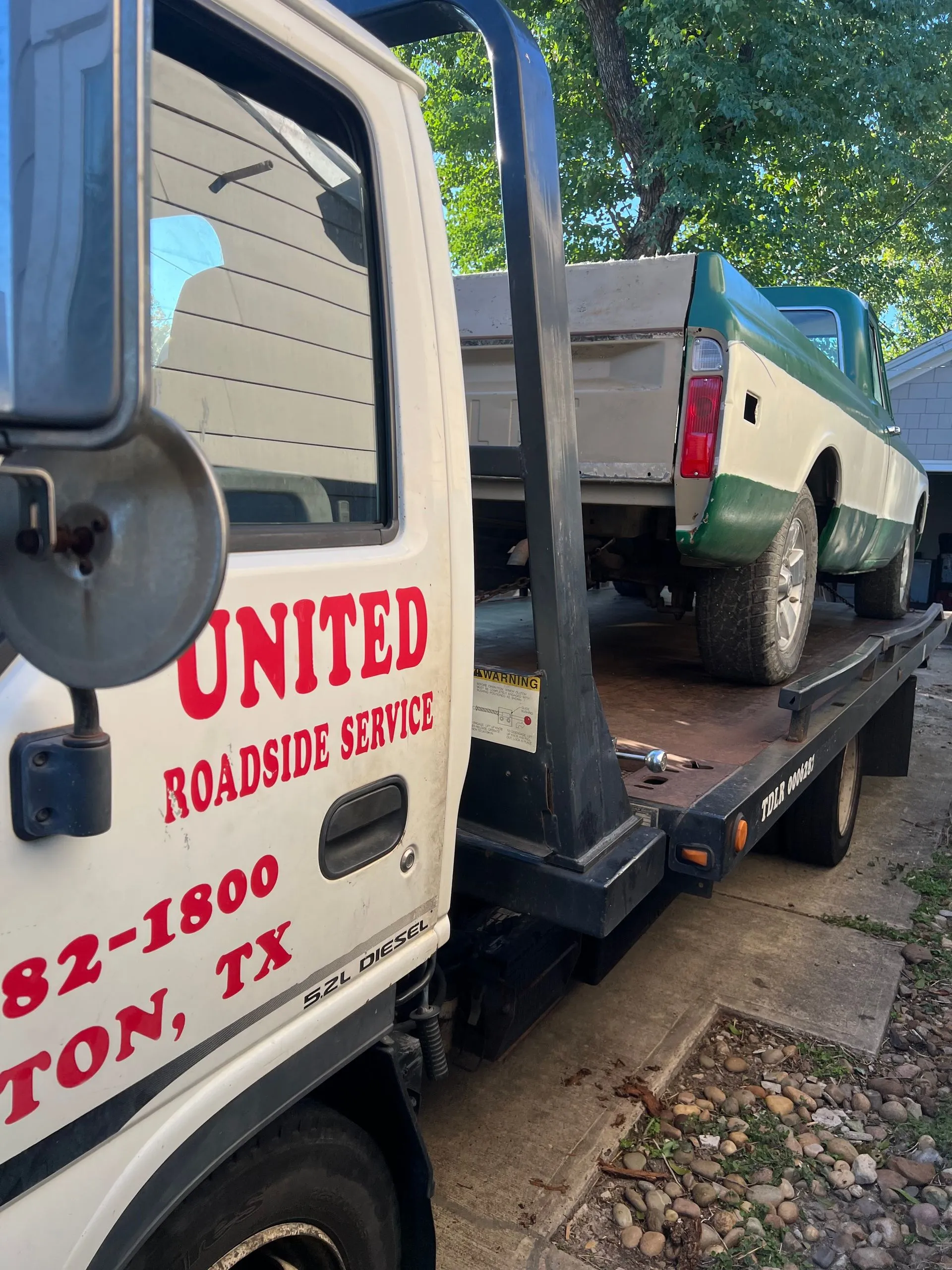 United Roadside Service transports a classic green and white pickup truck on a flatbed, ensuring secure loading, dependable vehicle transportation, professional towing, reliable roadside assistance, and careful automotive handling.