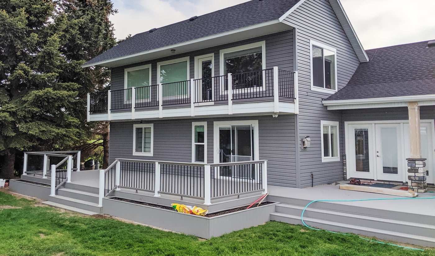 Transform your home's exterior with a complete multi-level outdoor living solution from DeckPro LLC. This project features a private second-story balcony and an expansive lower deck with custom built-in planters, all built with durable grey composite decking and modern railing.