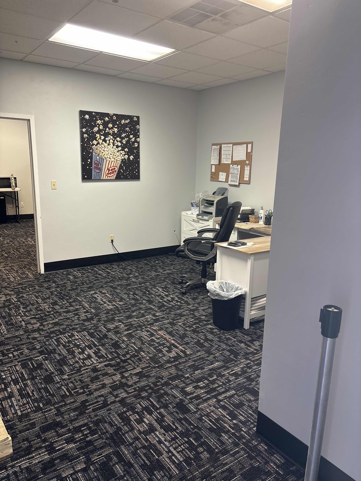 An office interior with a popcorn-themed painting on the wall, a desk with a computer and office sup 