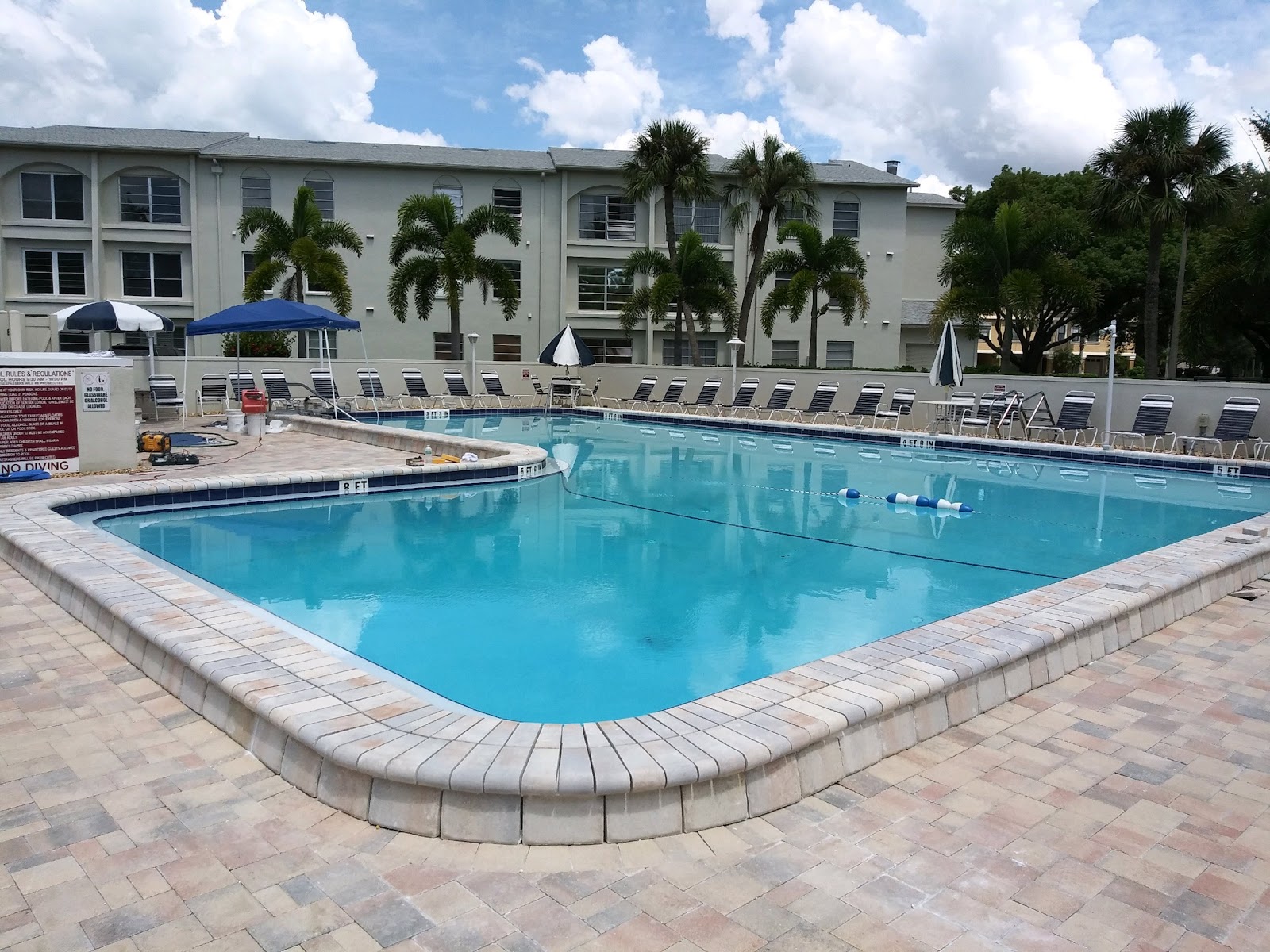 Resort-style community pool with spacious paver decking and residential buildings in the background.