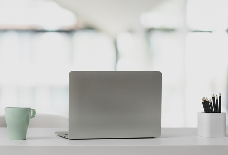 A desk with a laptop, mug, and container of pencils on it.