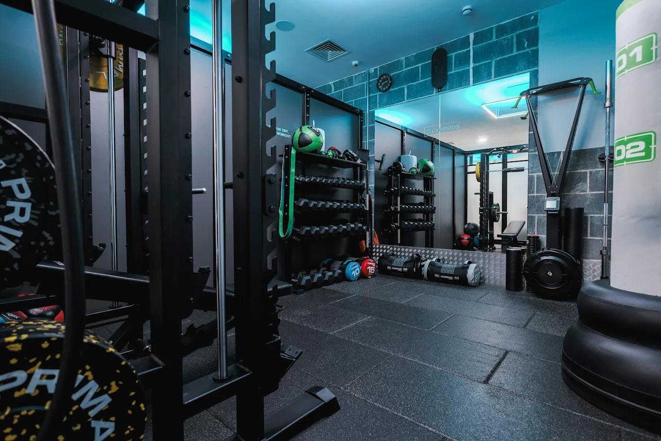 Private GYMPODS Putney gym pod with squat rack, dumbbells, bench and strength equipment in a modern, mirrored training space.