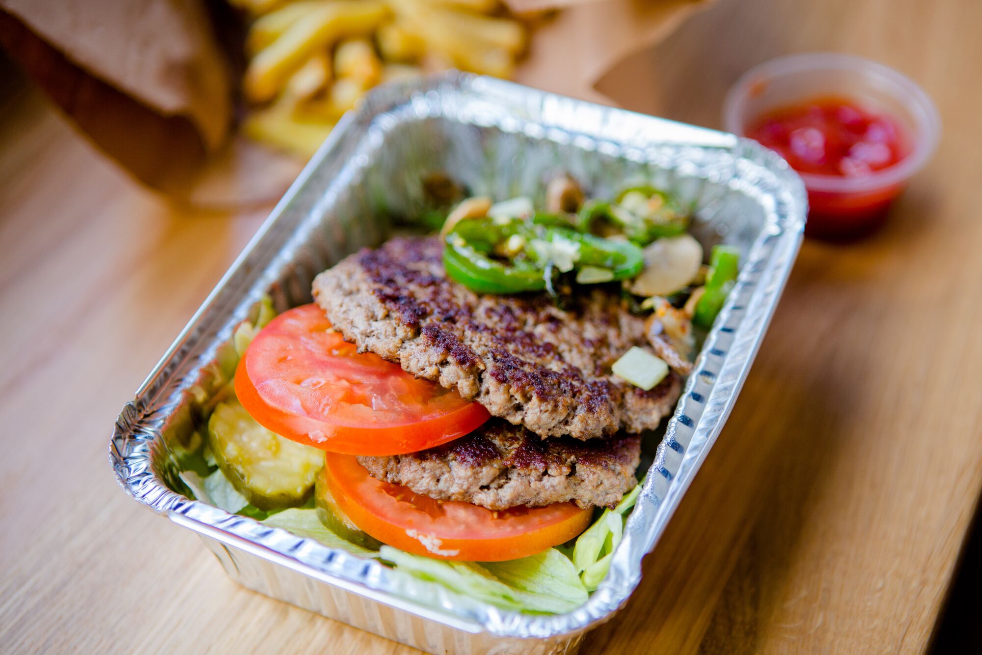 A photograph of the contents of a Five Guys burger bowl, which include two ground beef patties, tomatoes, jalapenos, lettuce and pickles.