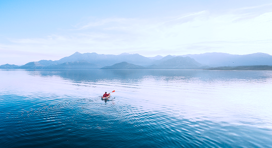 Person kayaking on a lake with a foggy mountain view.