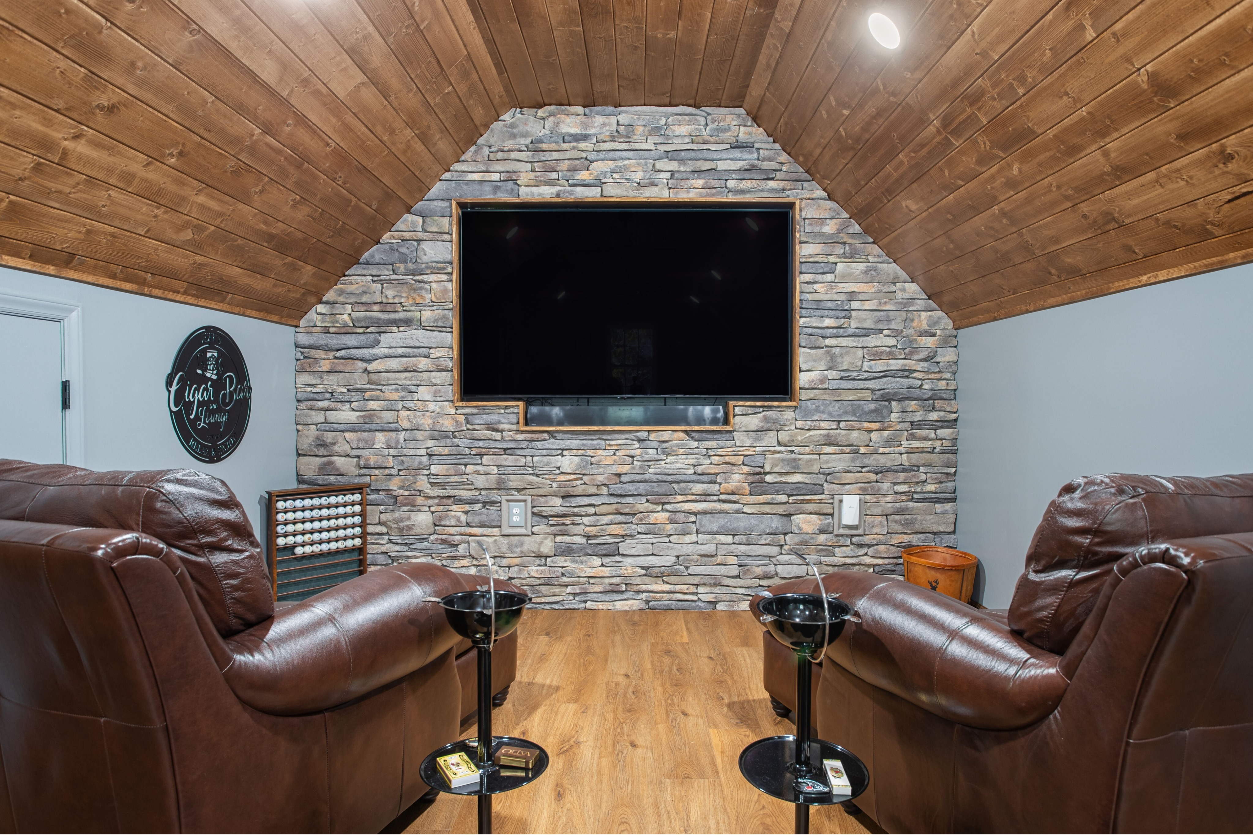 Luxury finished entertainment room in Central North Carolina with a custom wood ceiling, stone fireplace accent wall, and built-in media area. Designed and built by an experienced residential contractor specializing in custom home remodeling and interior construction.