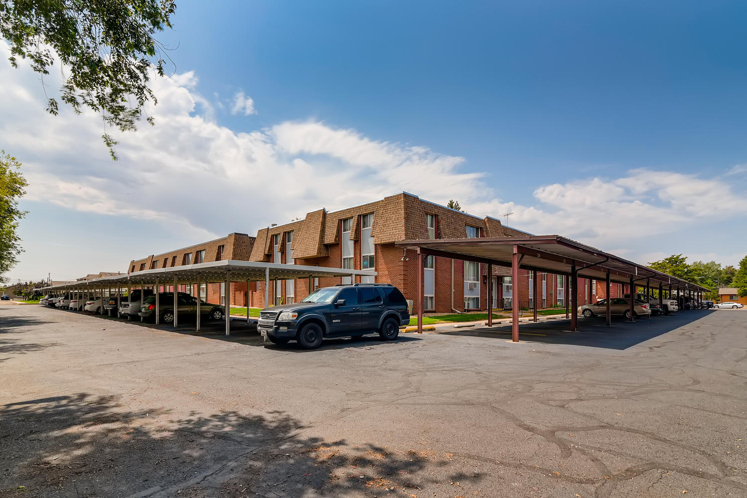 Parking lot with covered parking and brick and siding building exterior in background.