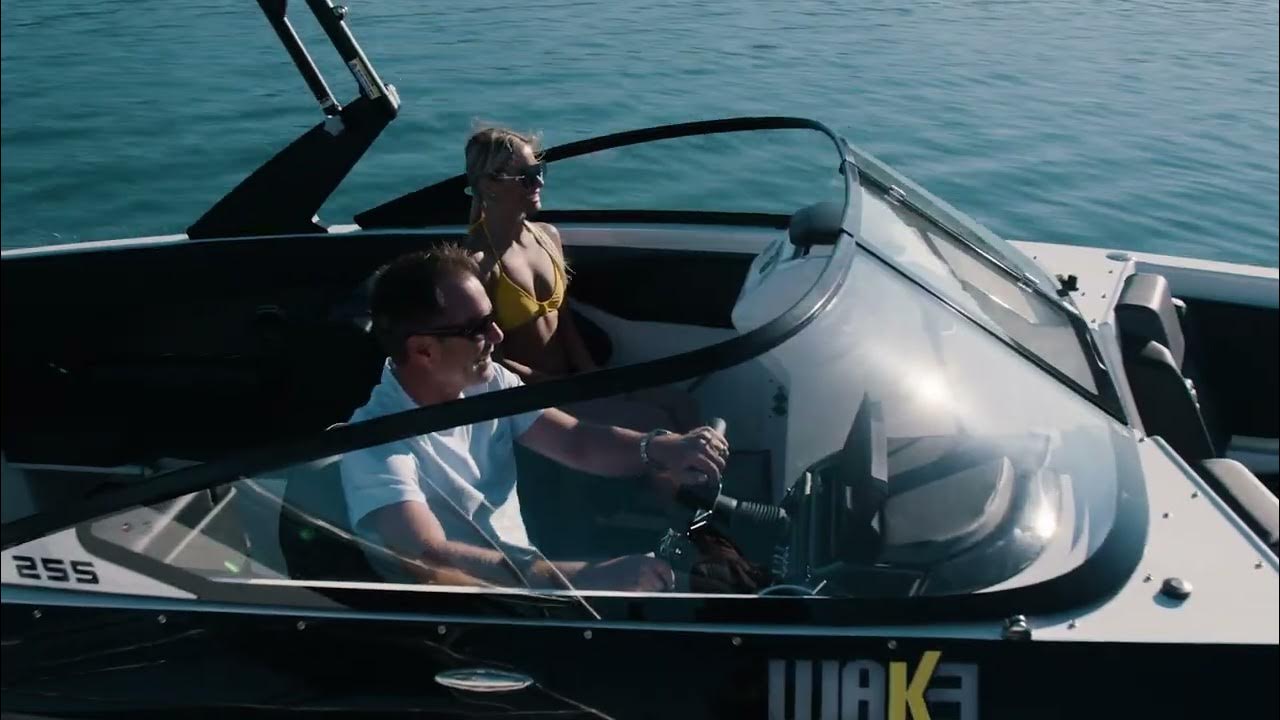 A man and a woman are on a boat in the ocean. The man is driving the boat and the woman is sitting in the passenger seat. The boat is a white and black speedboat with a windshield. The water is blue and there are some small waves. The sky is also blue and there are some clouds.