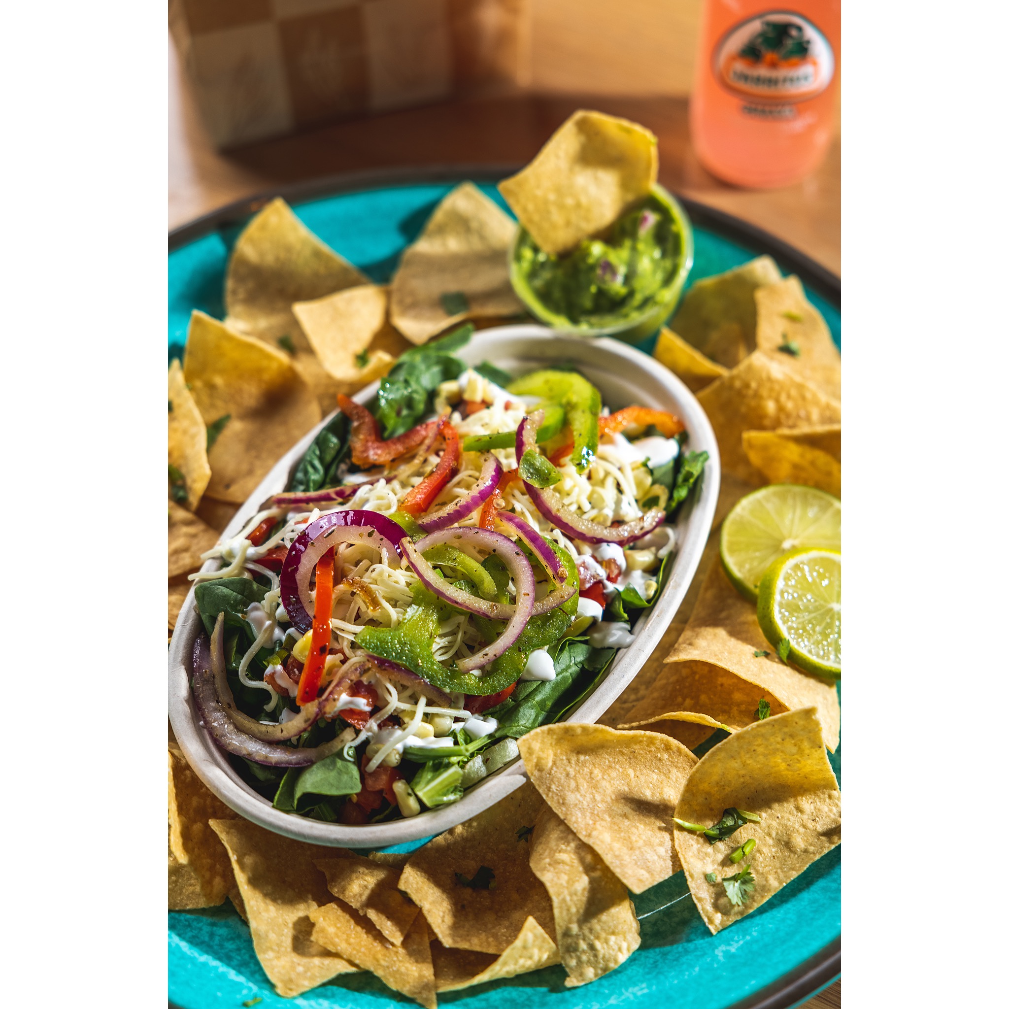 bowl with rice, beans, chicken, and toppings, with chips and a Jarritos drink 