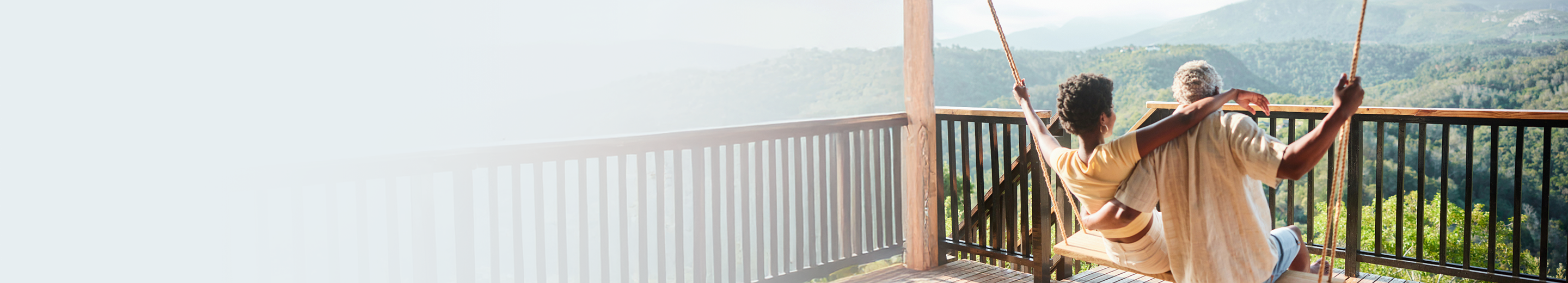 A mature couple on a patio swing looking out over a forest.