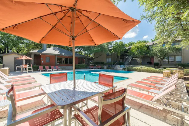 Swimming pool with striped lounge chairs under orange umbrella at The Colony Apartments