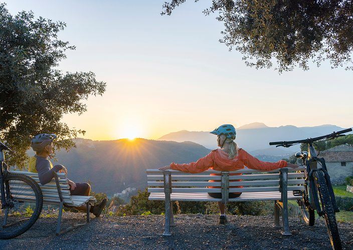 A couple taking a break from their bike ride while enjoying a scenic view of the sunrise.